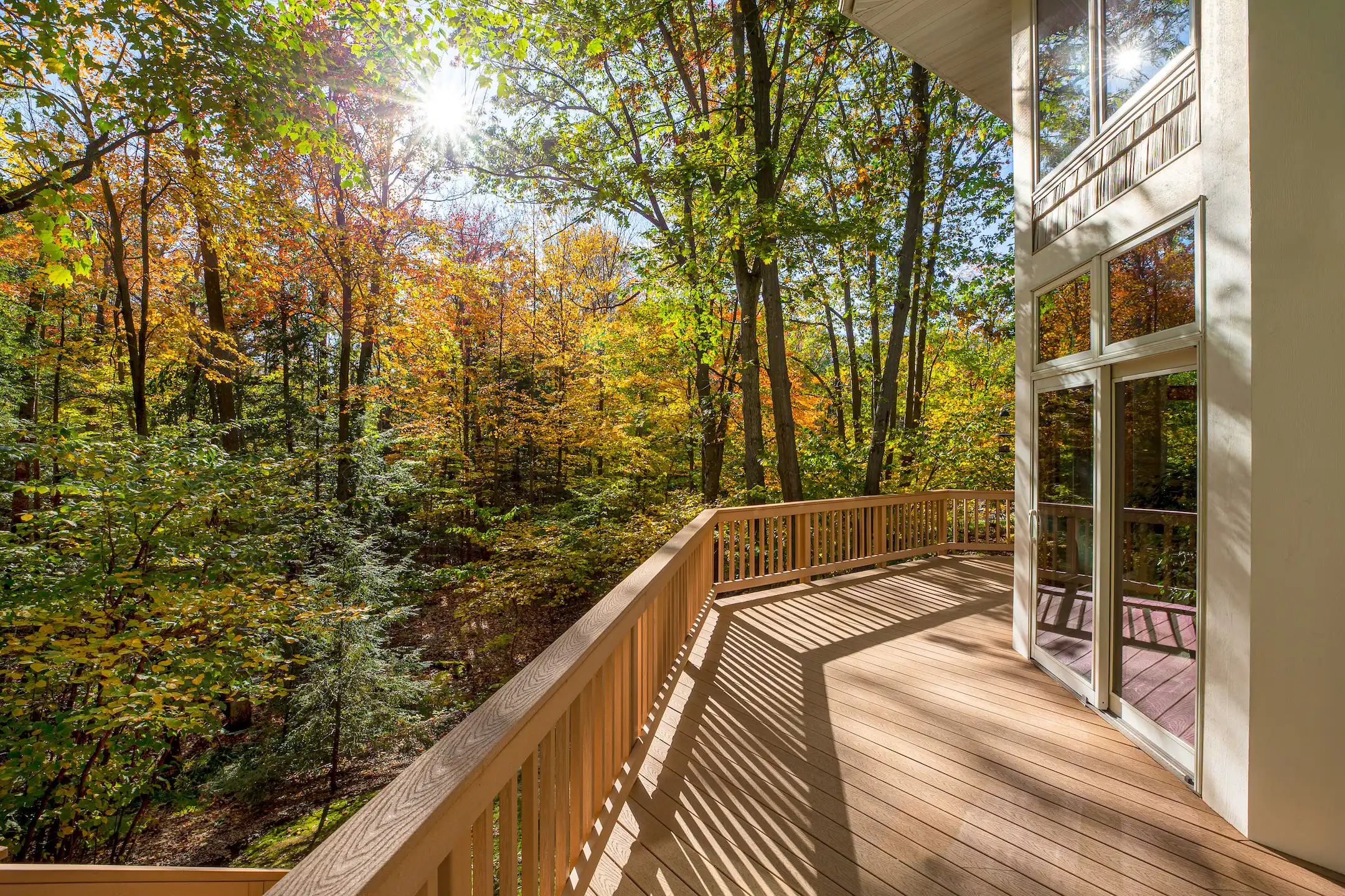 View from the deck of a luxury home in the autumn woods.  Outdoor living concept, bright fall foliage, and intentional sun flare highlight.